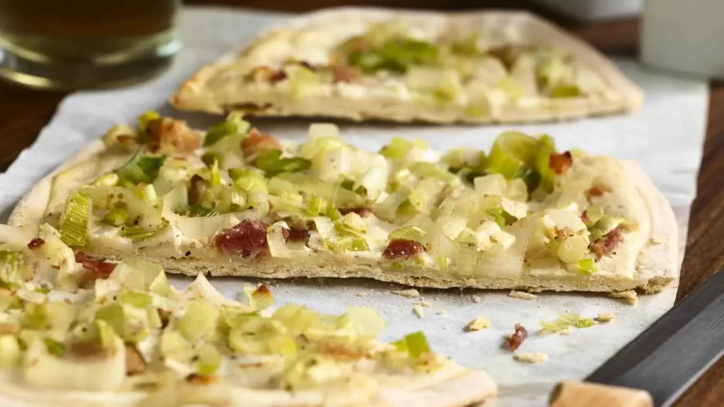 Flammkuchen in drei knusprige Stücke geteilt, belegt mit Speck und Zwiebeln.