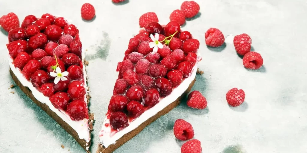 Zwei Himbeer-Schmand-Kuchen, die in Herzform arrangiert sind, dekoriert mit frischen Himbeeren.