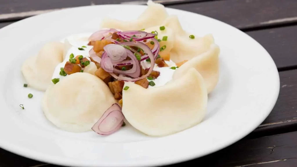 Servierte Piroggen mit Zwiebeln, Speckwürfeln und Sauerrahm auf einem weißen Teller