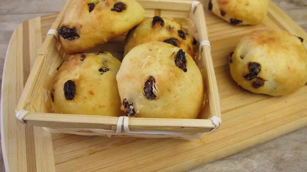 Goldbraune Rosinenbrötchen in einem Korb auf einem Holzbrett – Leckeres Rezept zum Selberbacken