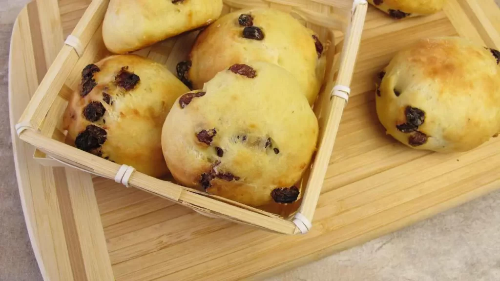 Frisch gebackene Rosinenbrötchen in einem Holzkörbchen, perfekt für einen klassischen Snack zu Hause