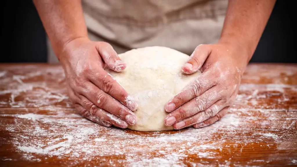 Bäcker formt Sauerteigbrotteig mit den Händen auf einer bemehlten Arbeitsfläche