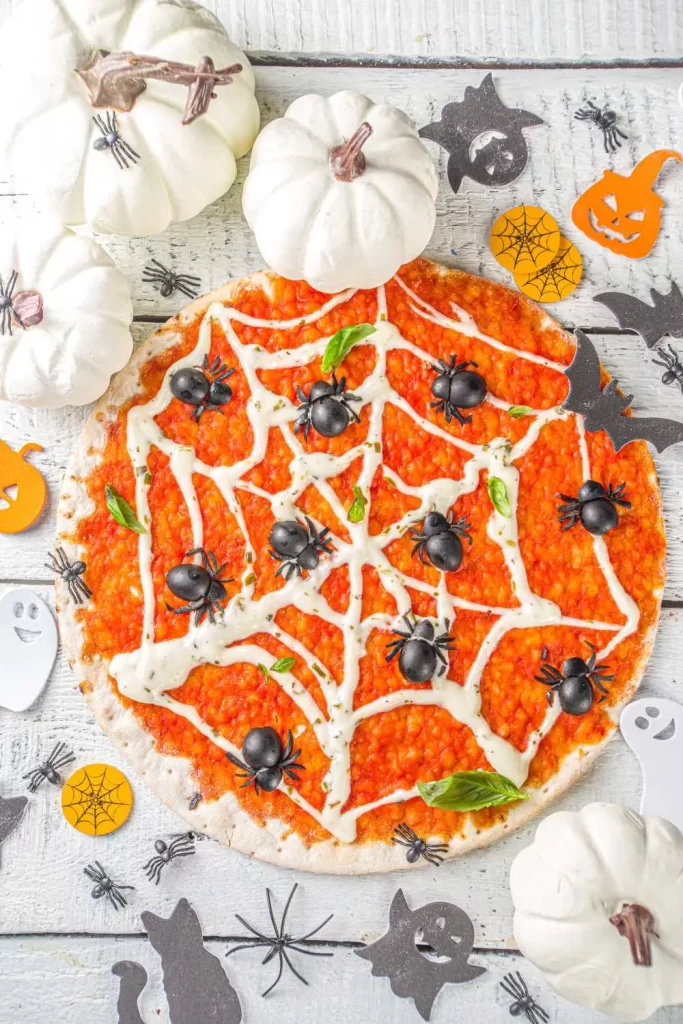 Halloween-Pizza für die Party mit gruseligen Motiven wie Kürbisgesichtern und Olivenspinnen