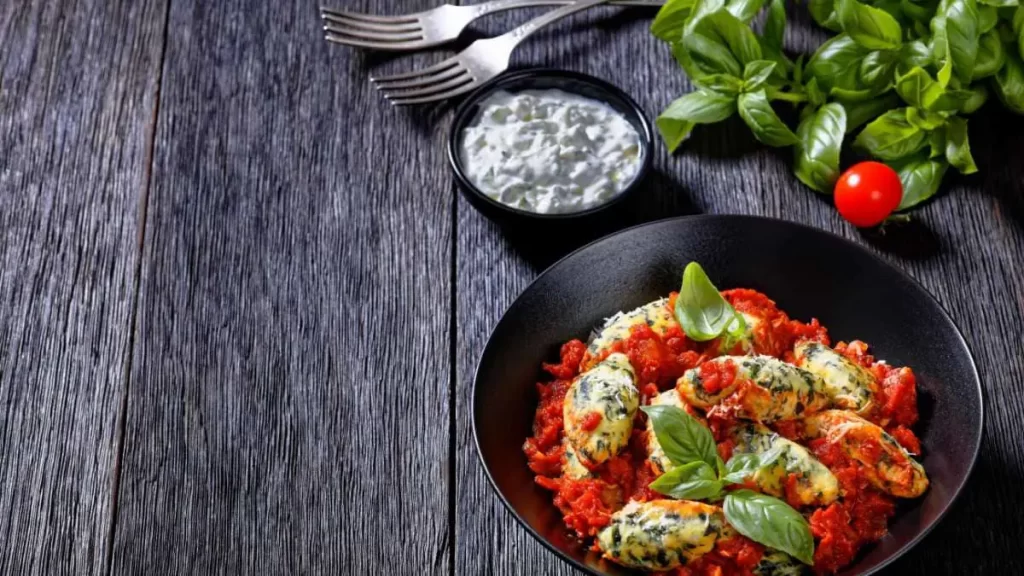 Malfatti mit Tomatensauce, garniert mit frischem Basilikum und Parmesan