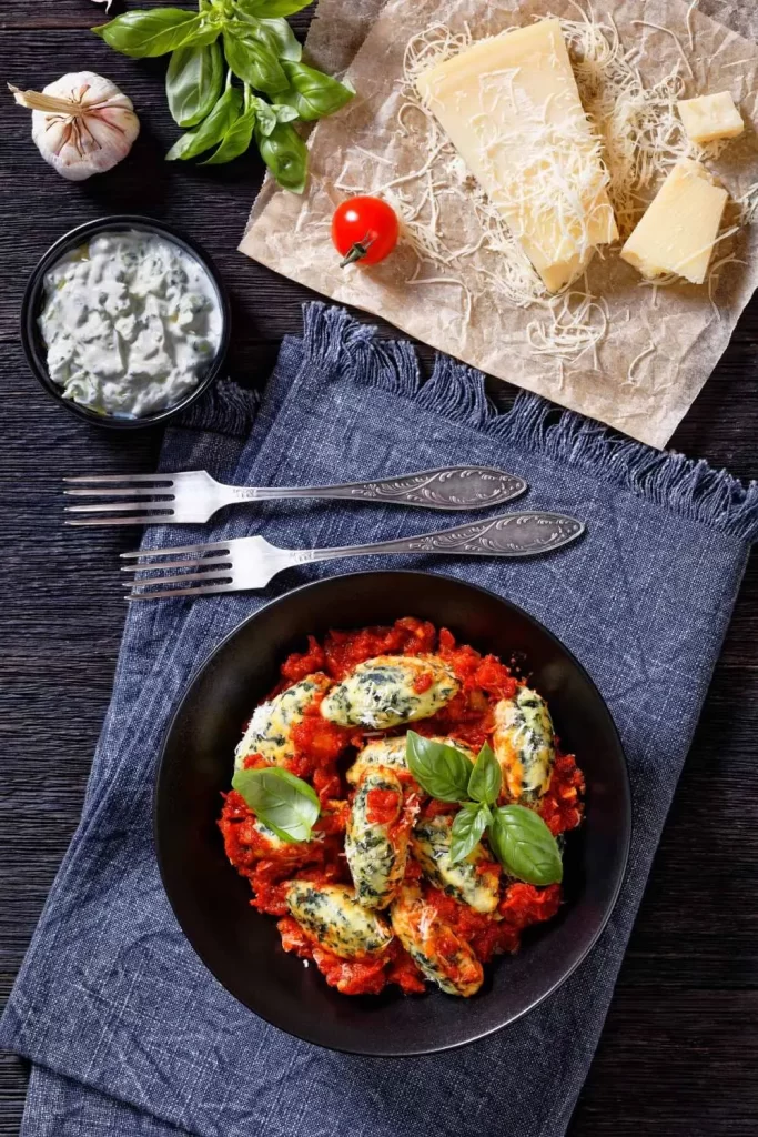  Malfatti mit Tomatensauce, garniert mit geriebenem Parmesan und frischem Basilikum