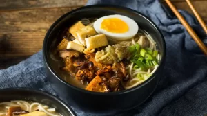 Schüssel mit dampfendem vegetarischem Ramen, frischem Gemüse und Nudeln in aromatischer Brühe