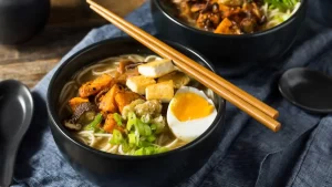 Schüssel mit traditioneller japanischer Suppe, gefüllt mit frischem Gemüse, Tofu und Kräutern in klarer Brühe