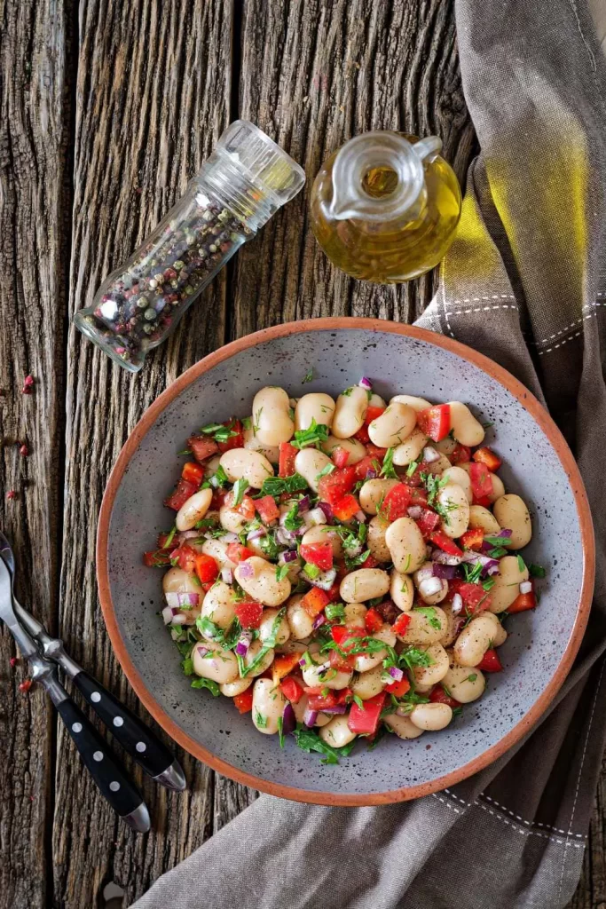 Veganer Salat aus weißen Bohnen mit Tomaten, Gurken, roten Zwiebeln und frischem Kräuterdressing