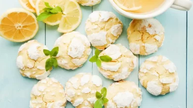 Frische, goldbraune Zitronenkekse auf einem Holztisch, garniert mit Zitronenscheiben und Puderzucker