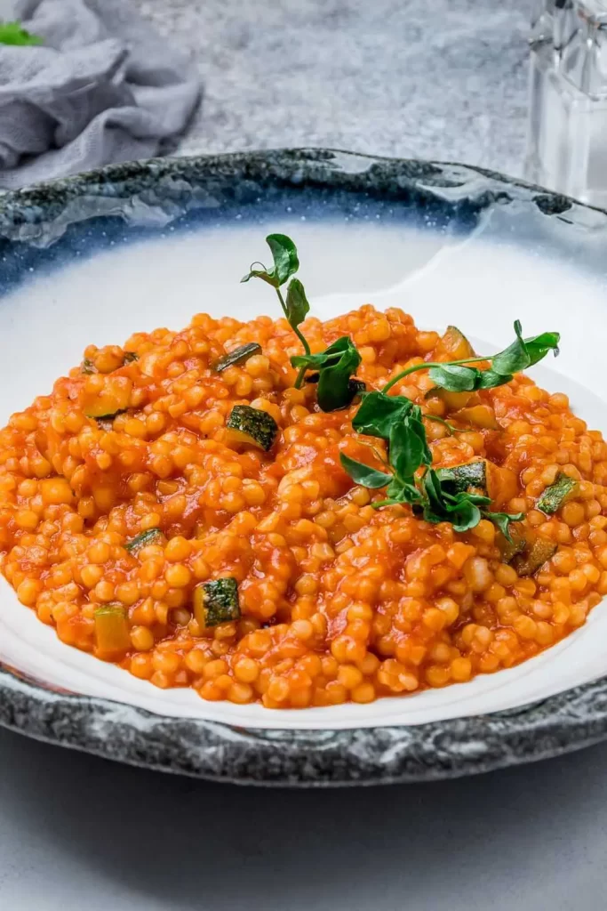 Klassische Fregola Sarda, goldbraune Kügelchen aus Pasta, serviert mit einer Tomatensauce und Kräutern